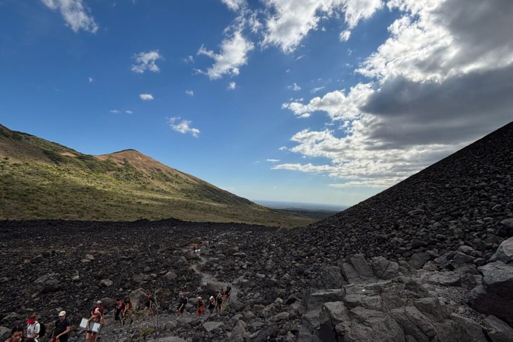 Hikers climbing the black volcanic rock slopes of Cerro Negro Volcano near León, Nicaragua, with expansive views across the surrounding landscape.