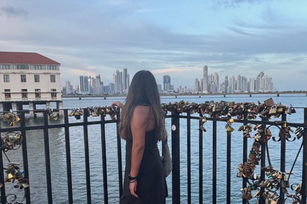 Traveler looking across Panama Bay toward the Panama City skyline from the Cinta Costera waterfront, with hundreds of love locks attached to the railing in the foreground.