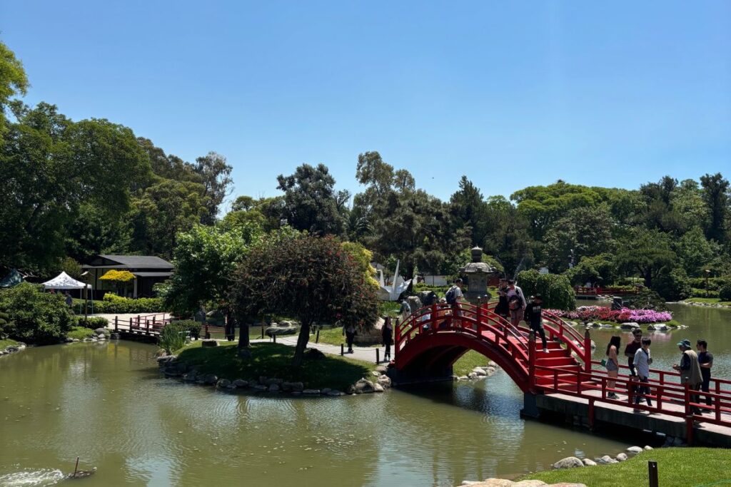 Japanese Garden in Buenos Aires with a red arched bridge, pond, trees, and visitors.
