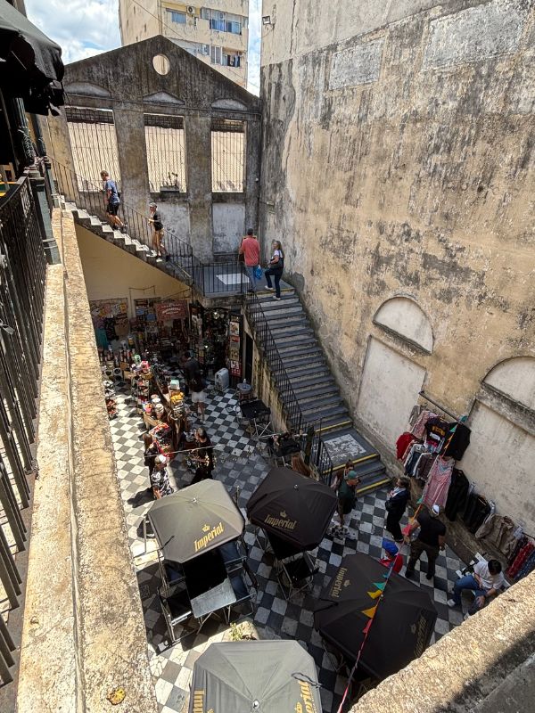 San Telmo market courtyard with checkered flooring, vendor stalls, café umbrellas, and staircases.