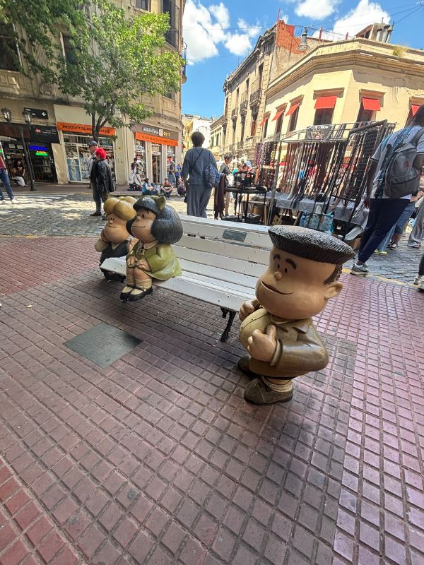Mafalda comic character statues seated on a bench along a lively street in San Telmo, Buenos Aires.