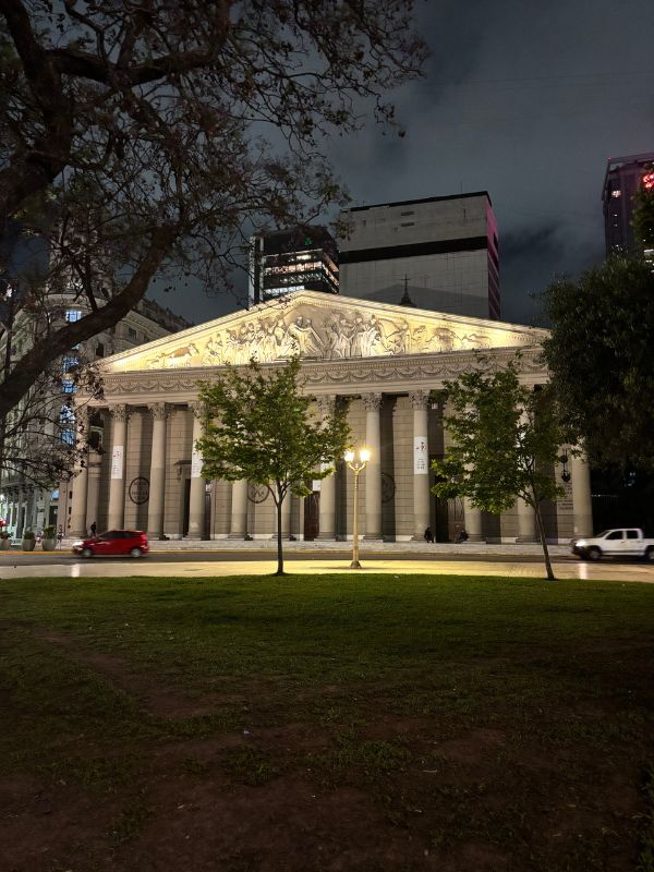 Buenos Aires Metropolitan Cathedral illuminated at night, framed by trees and surrounding city buildings.