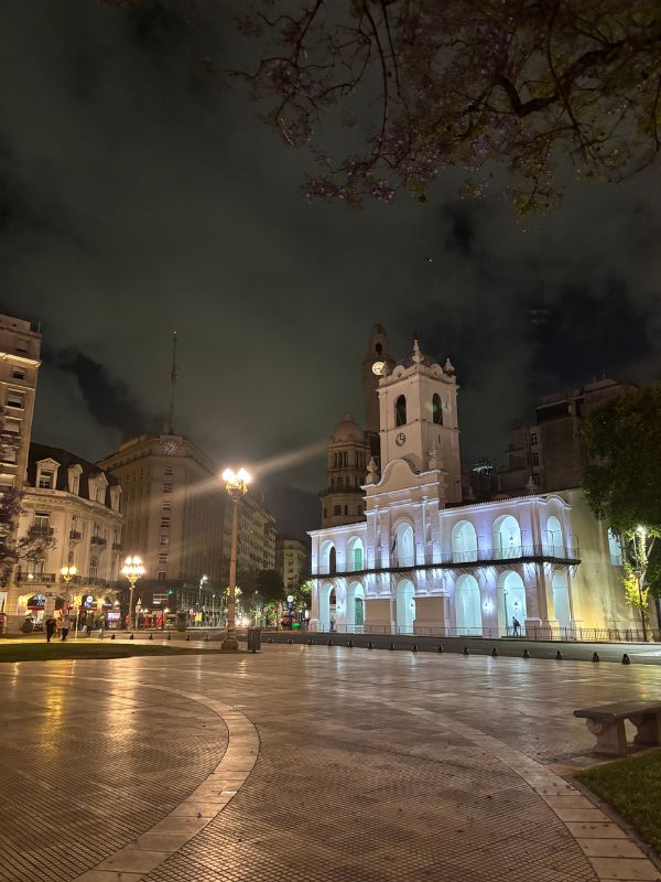 Cabildo of Buenos Aires illuminated at night in Plaza de Mayo beneath a cloudy sky.