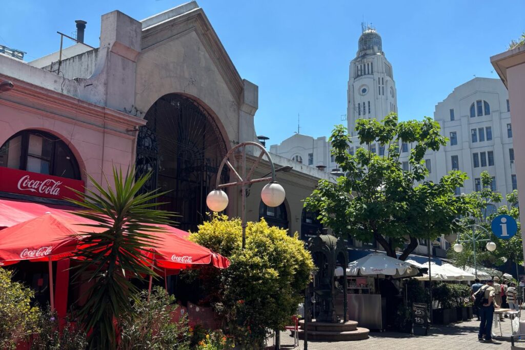 Mercado del Puerto in Montevideo with outdoor cafés and the Palacio Salvo visible in the background under a clear blue sky.