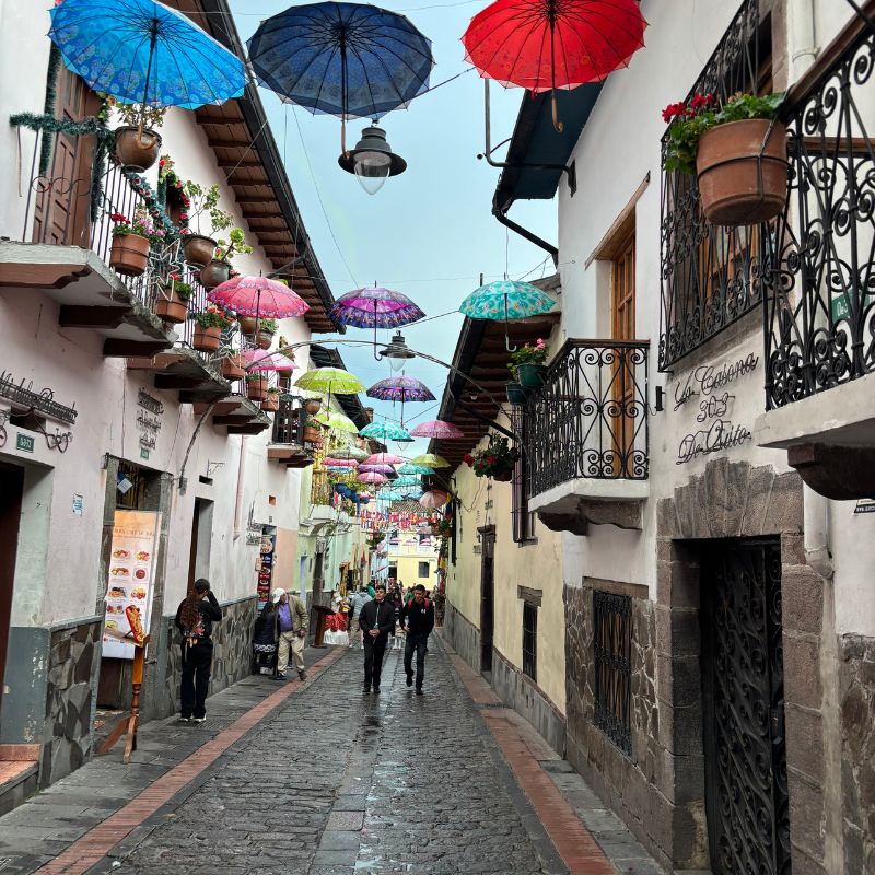 Colorful umbrellas suspended above a narrow colonial street in Quito's Historic Center, Ecuador.